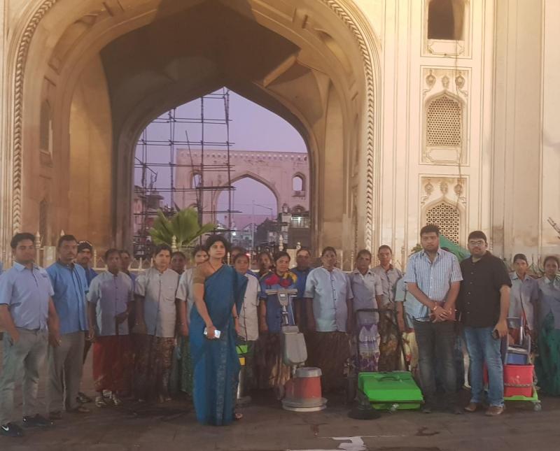 Ixora team group photo at Charminar heritage site with cleaning equipment